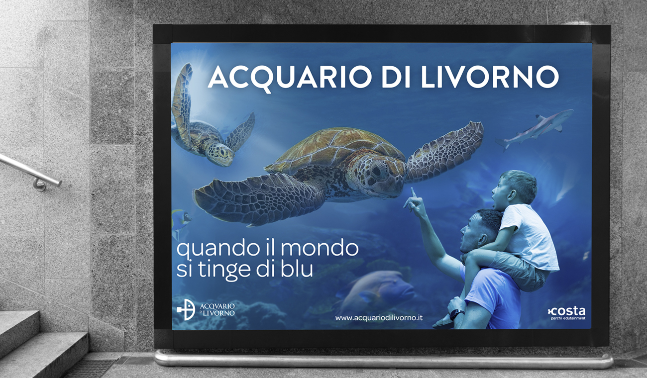 nell'immagine c'è un papà e un bambino che guardano tartarughe giganti e altre creature. Questa è la campagna dell'Acquario di Livorno 2023 fatta da Rebel Studio